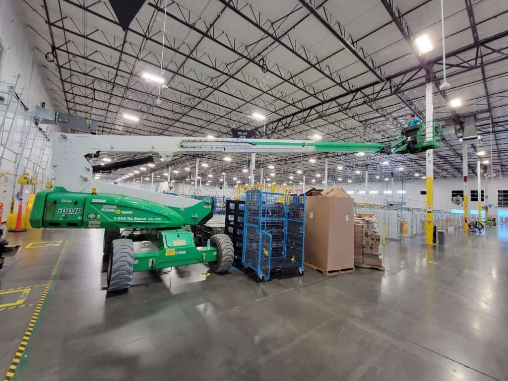 Articulating boom lift extended for ceiling electrical work in a warehouse