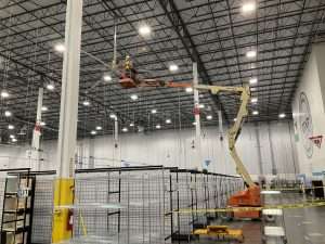 Boom lift installing a ceiling fan in a distribution center