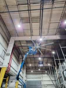 Boom lift installing a ceiling fan in a high bay facility
