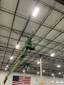 Electrician on a boom lift doing electrical work at a high warehouse ceiling