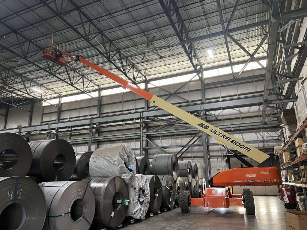 Boom lift raised for overhead electrical work above steel coils in a plant