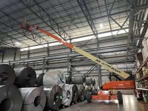 Boom lift raised for overhead electrical work above steel coils in a plant