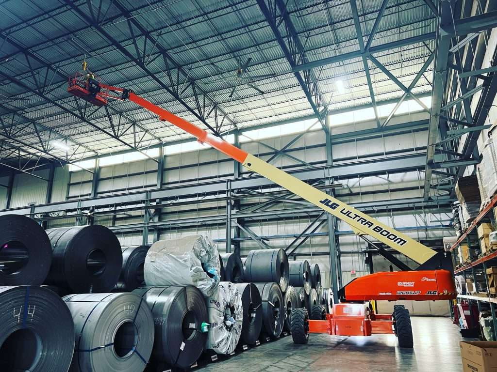 Boom lift performing electrical installation above steel coils in a warehouse