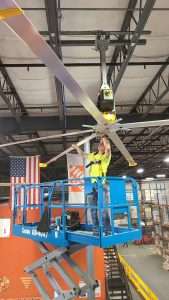 Electrician on a scissor lift mounting an HVLS fan to a warehouse ceiling