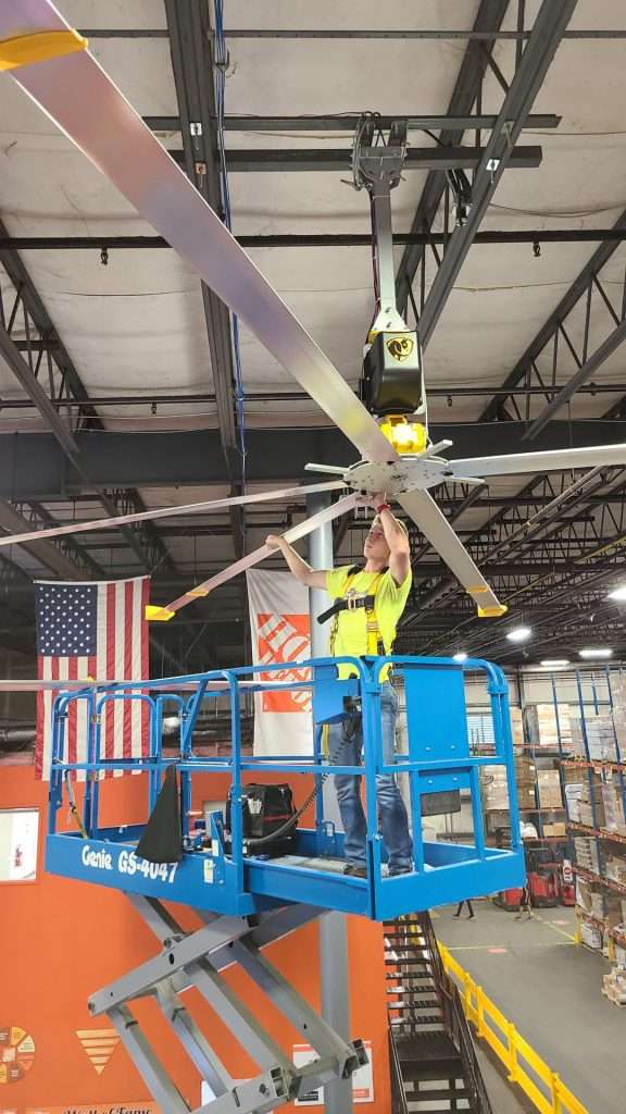 Electrician on a scissor lift mounting an HVLS fan to a warehouse ceiling