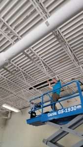 Electrician on a scissor lift running wiring along a gym ceiling