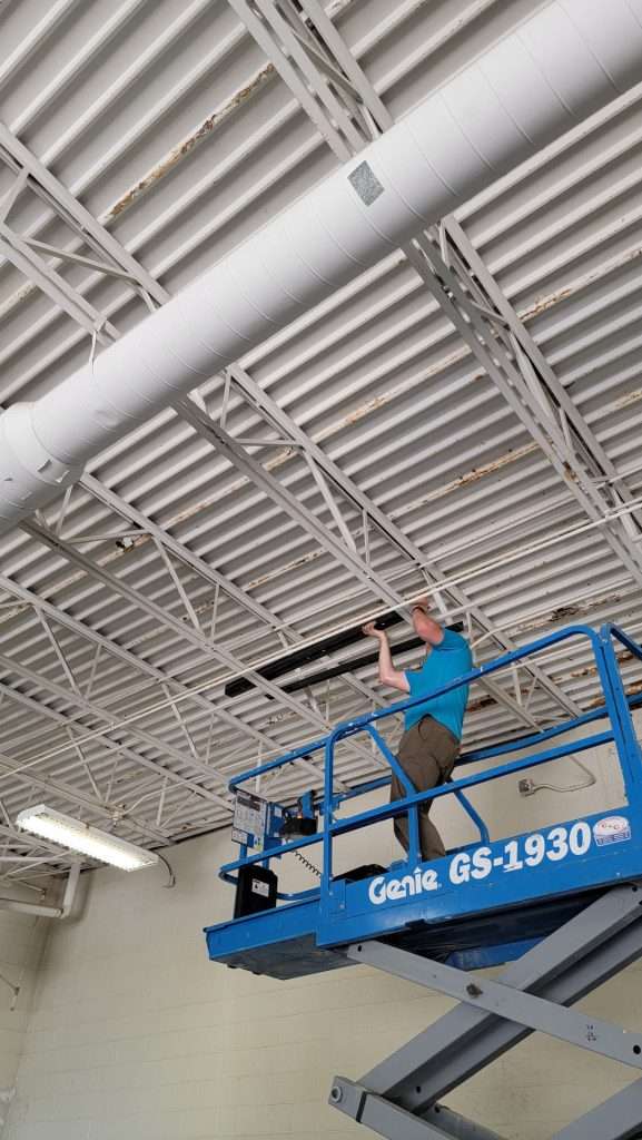 Electrician on a scissor lift running wiring along a gym ceiling
