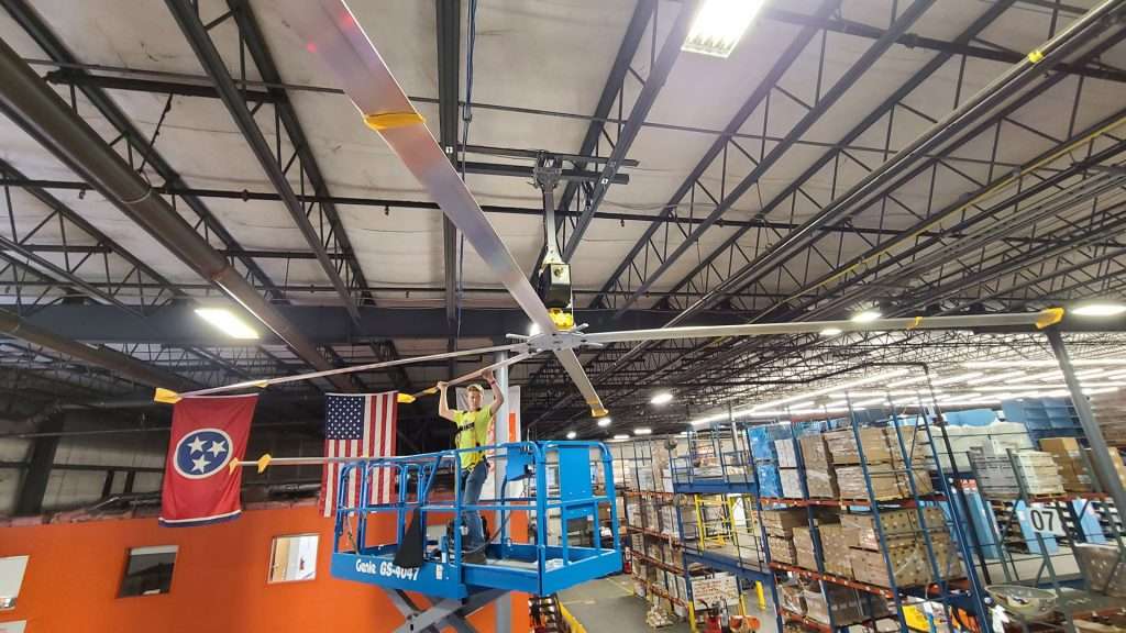 Electrician on a scissor lift installing an industrial ceiling fan in a warehouse