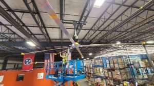 Electrician on a scissor lift installing an industrial ceiling fan in a warehouse