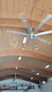 Large industrial ceiling fan mounted on a wood ceiling in a gymnasium