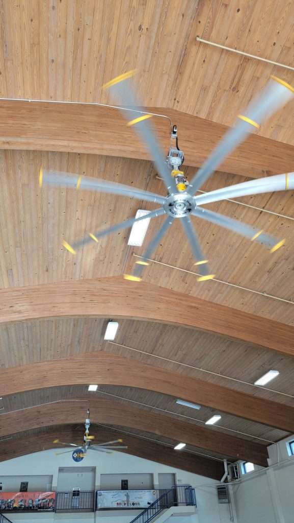 Large industrial ceiling fan mounted on a wood ceiling in a gymnasium