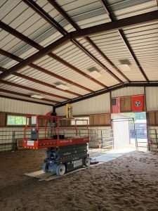 Scissor lift staged for electrical installation inside a covered livestock arena