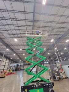 Scissor lift extended to the high bay ceiling for an electrical installation in a warehouse