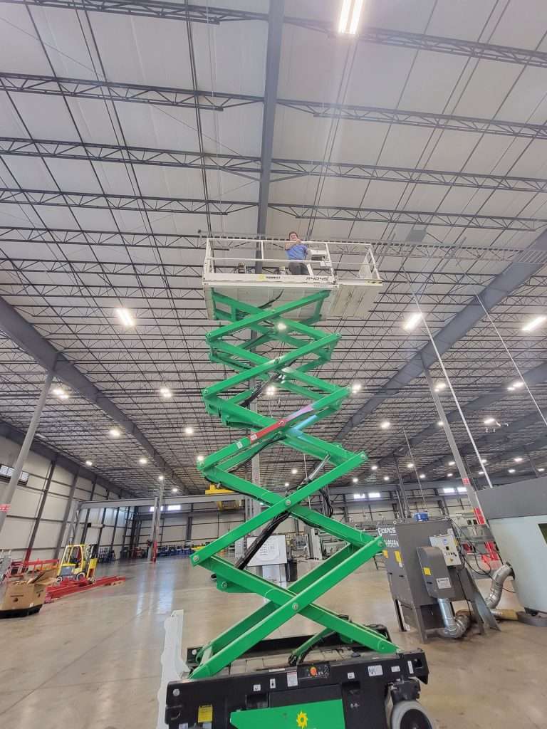 Scissor lift extended to the high bay ceiling for an electrical installation in a warehouse