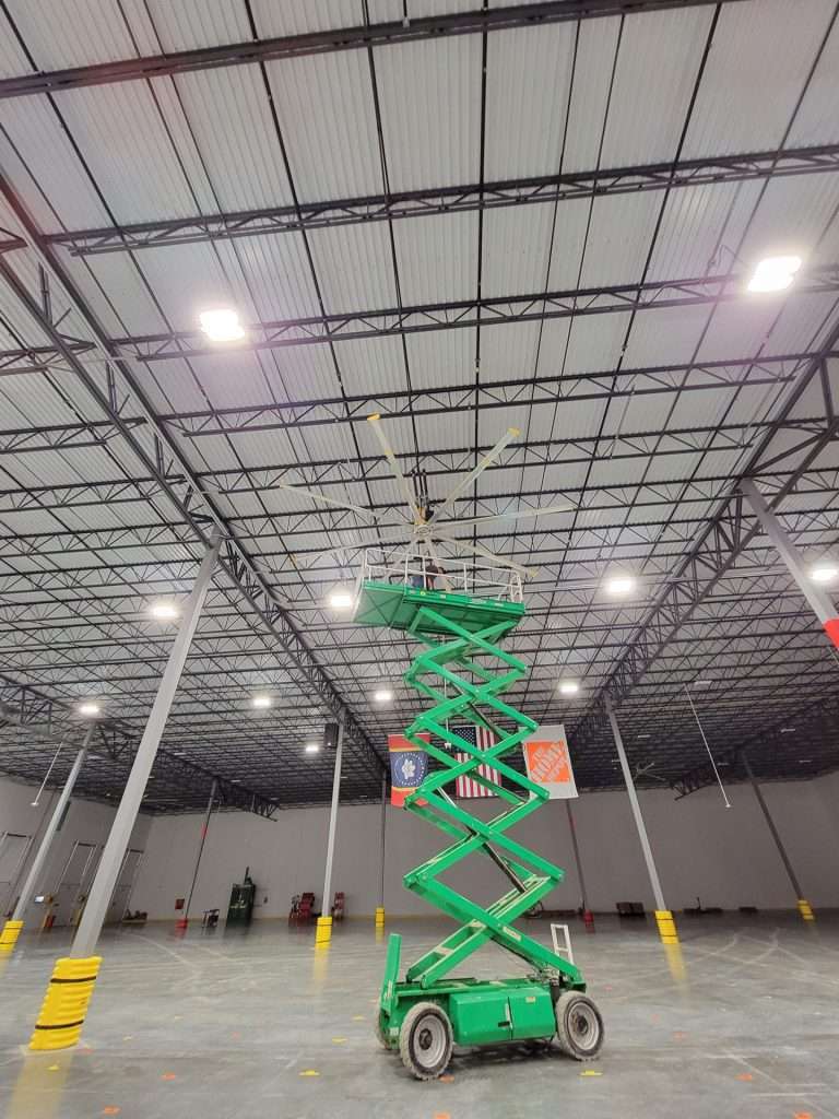 Green scissor lift raised to install an HVLS ceiling fan in a new warehouse
