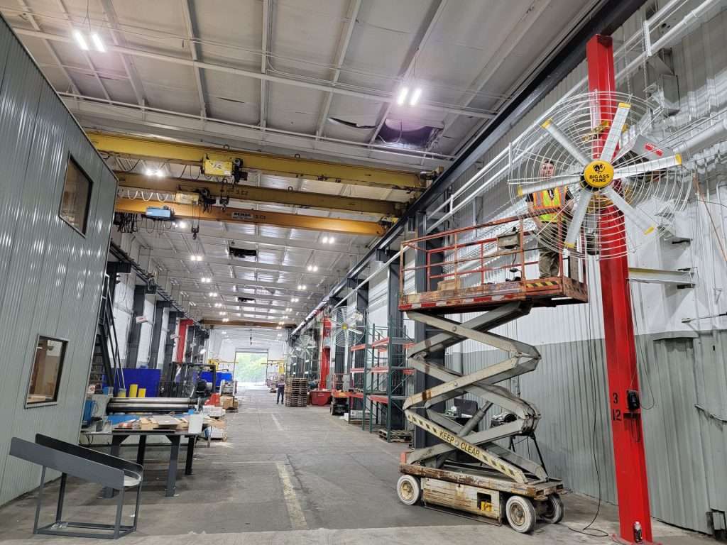 Wall-mounted industrial fan installed from a scissor lift inside a manufacturing shop